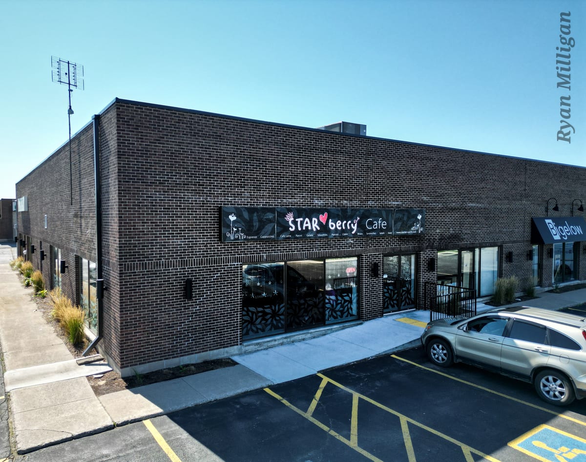 The corner of the brick commercial building at 450 Woodlawn Road West, the black Starberry Cafe sign above the windows and parking in front